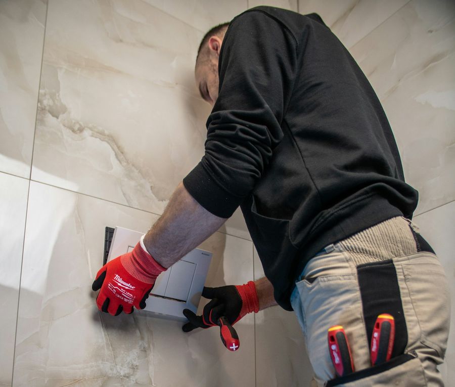 Plombier en gants de travail posant la plaque de commande d'un WC suspendu
