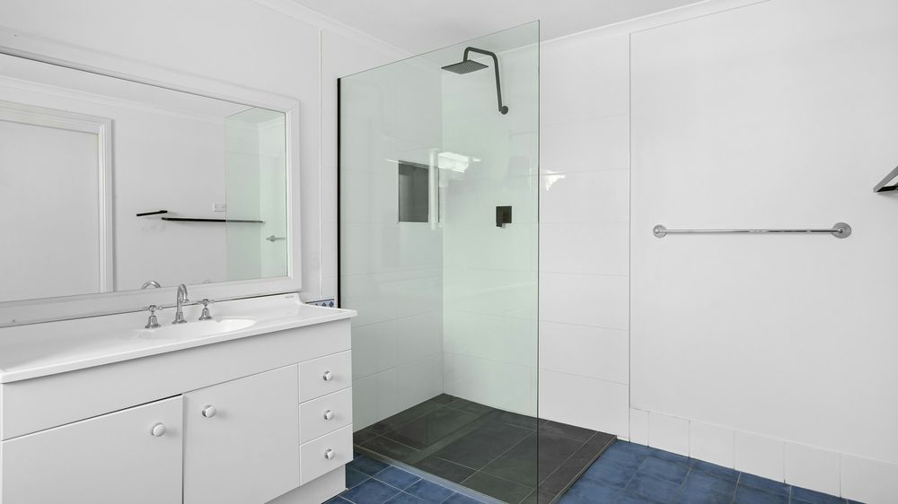 Salle de bain blanche avec douche de plain-pied, paroi vitrée et barre murale